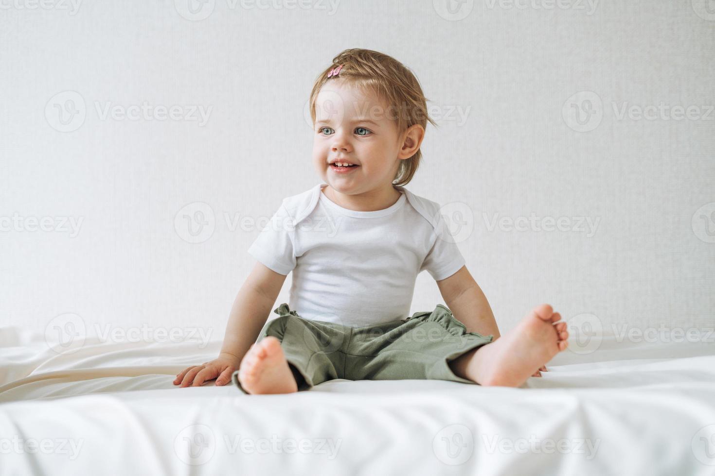 Cuty happy funny baby girl in home clothes sitting on bed at home photo