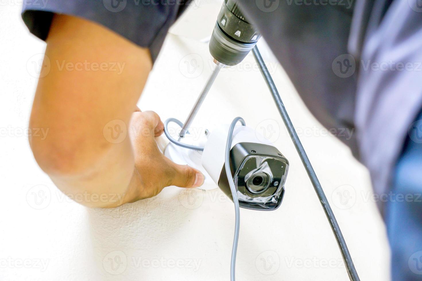 les mains du technicien utilisent un moteur électrique pour serrer l'écrou pour installer la cctv sur le mur du bâtiment. photo