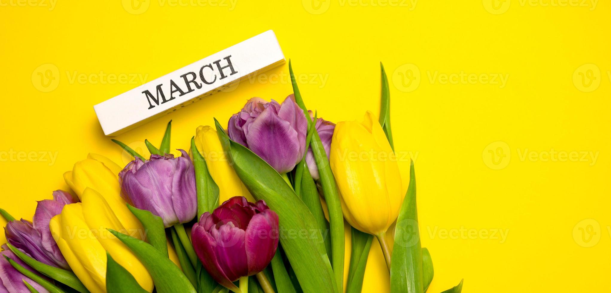 bannière de printemps. un bouquet de tulipes jaunes, roses et violettes et mars écrit sur un bloc de bois. concept de la journée de la femme photo