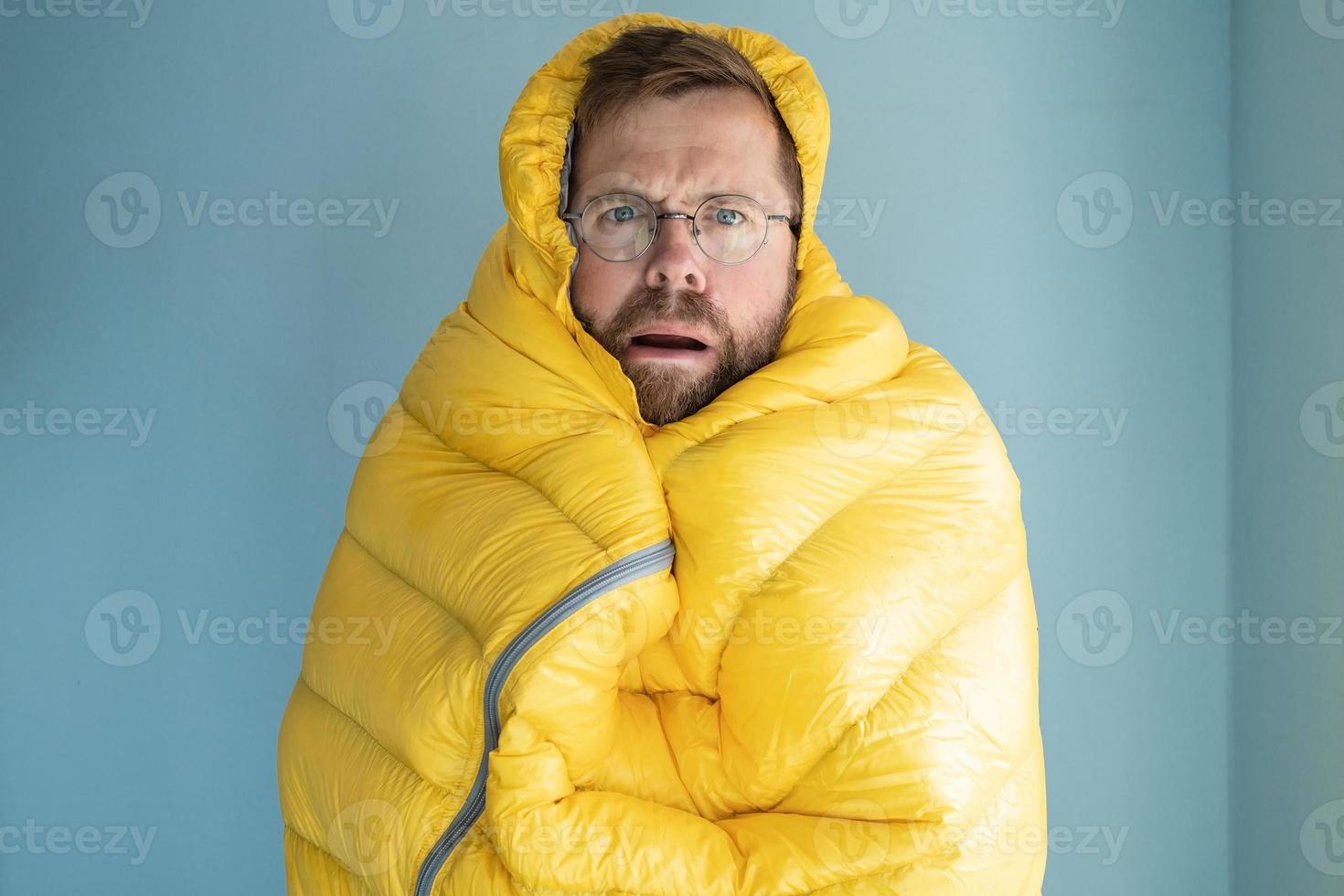 l'homme alarmé s'est figé et s'est enveloppé dans un sac de couchage chaud, debout à l'intérieur sur le fond d'un mur. concept de crise énergétique. photo