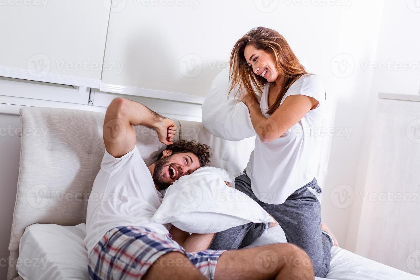 couple s'amusant pendant la bataille d'oreillers. jeune couple heureux a battu les oreillers sur le lit dans une chambre à la maison. photo