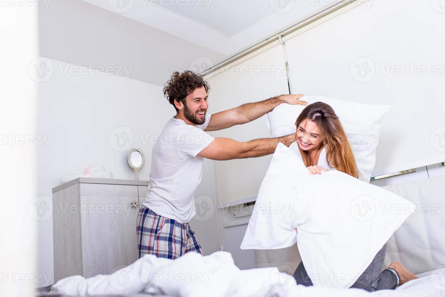 heureux jeune couple s'amuse au lit. appréciant la compagnie les uns des autres. bataille d'oreillers couple drôle se battant avec des oreillers au lit photo