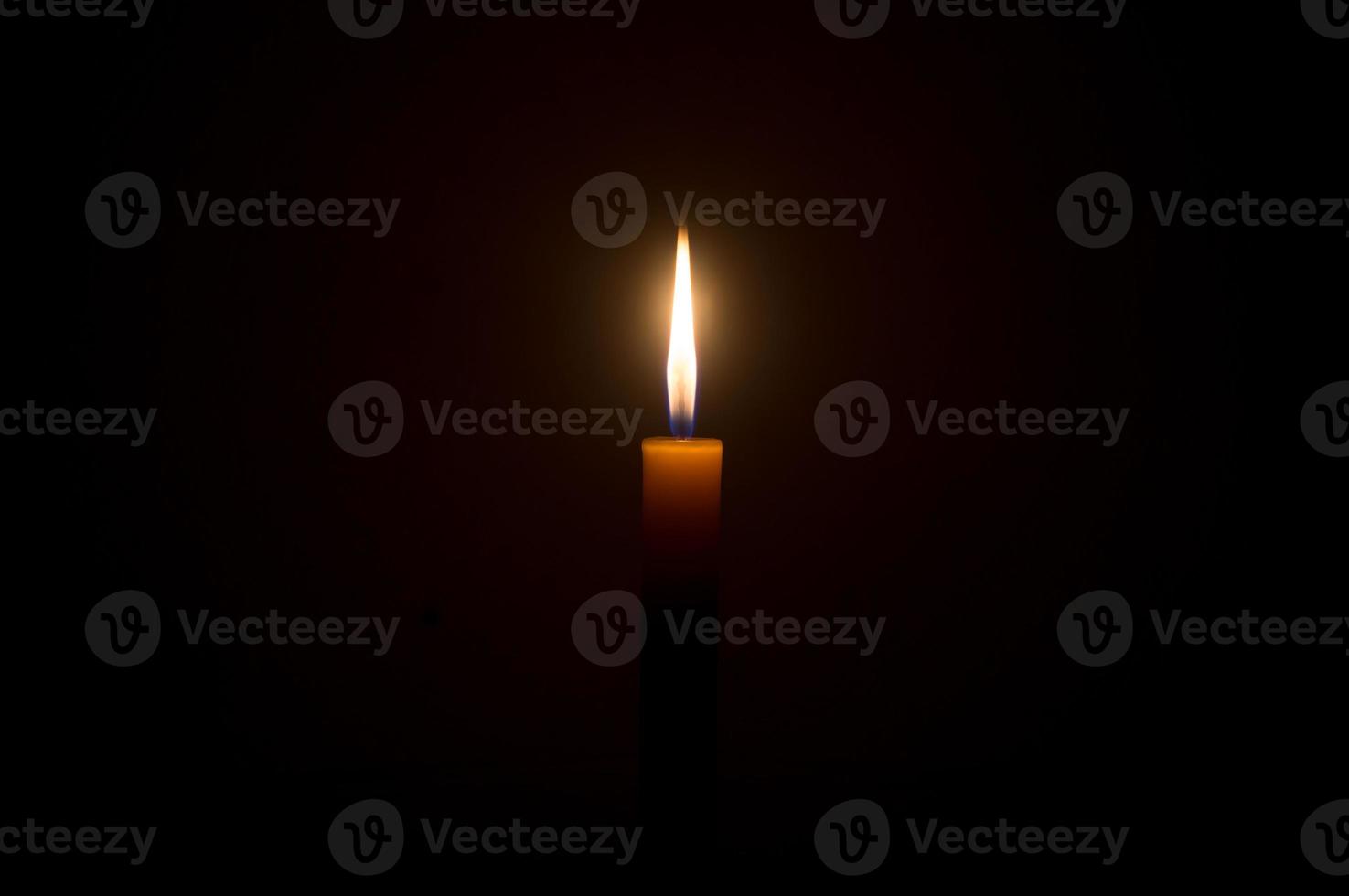 une seule flamme de bougie allumée ou une lumière rougeoyante sur une seule petite bougie jaune est isolée sur fond noir ou sombre sur la table de l'église ou du temple pour noël, les funérailles ou le service commémoratif photo