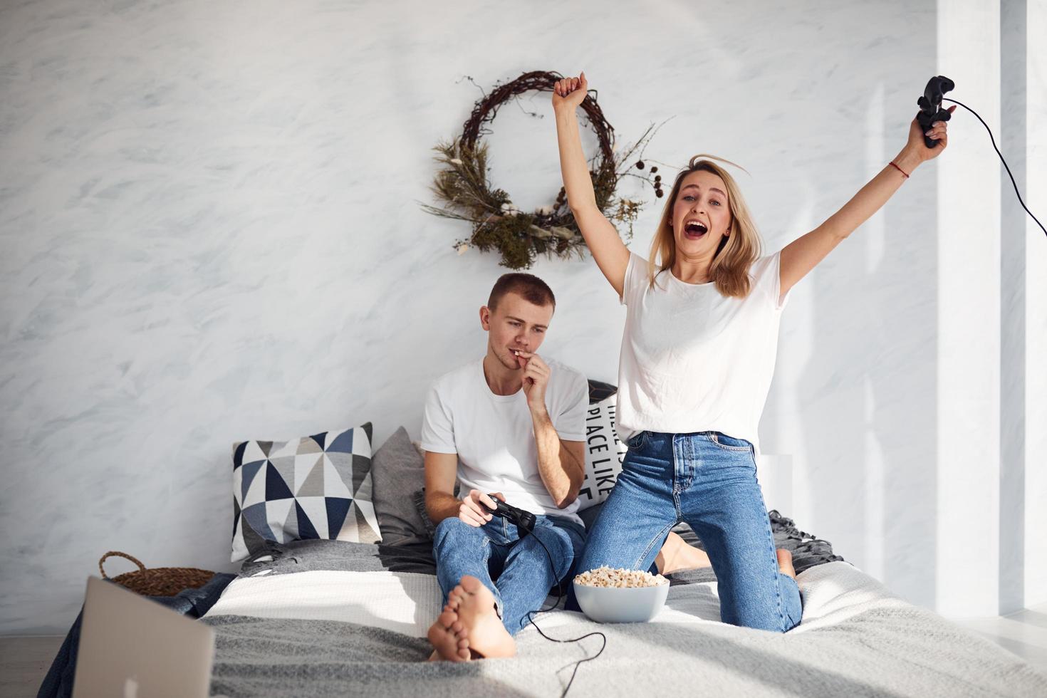 jeune couple charmant ensemble à la maison jouant à des jeux vidéo sur le lit avec du pop-corn le week-end photo