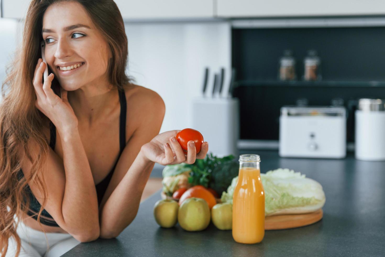 parle par téléphone. jeune femme européenne est à l'intérieur à la cuisine à l'intérieur avec des aliments sains photo