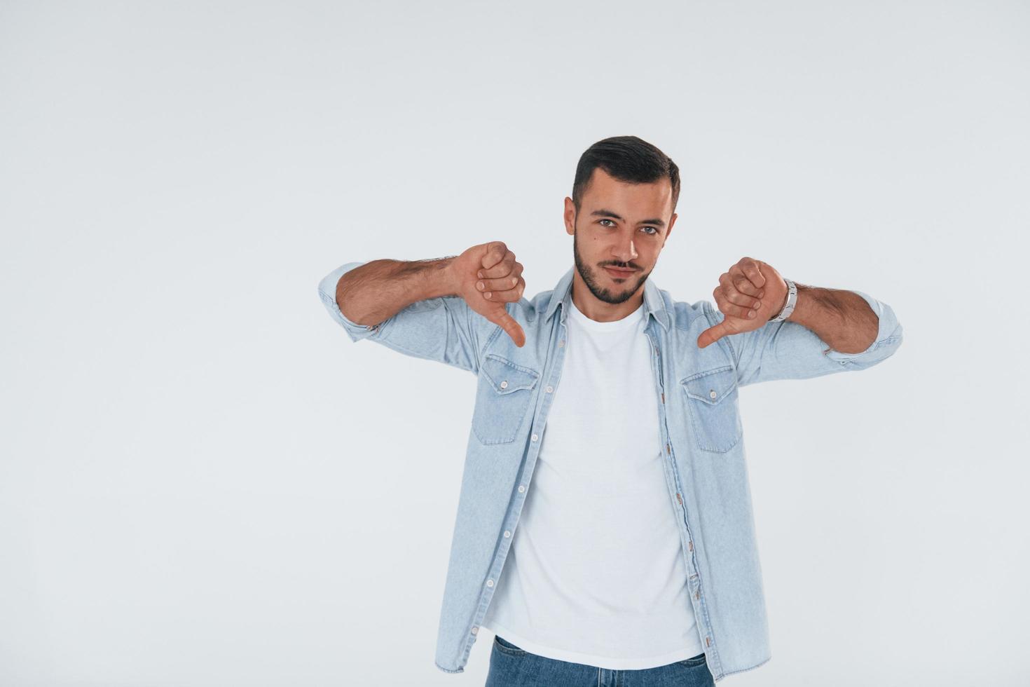 pouces vers le bas. jeune bel homme debout à l'intérieur sur fond blanc photo