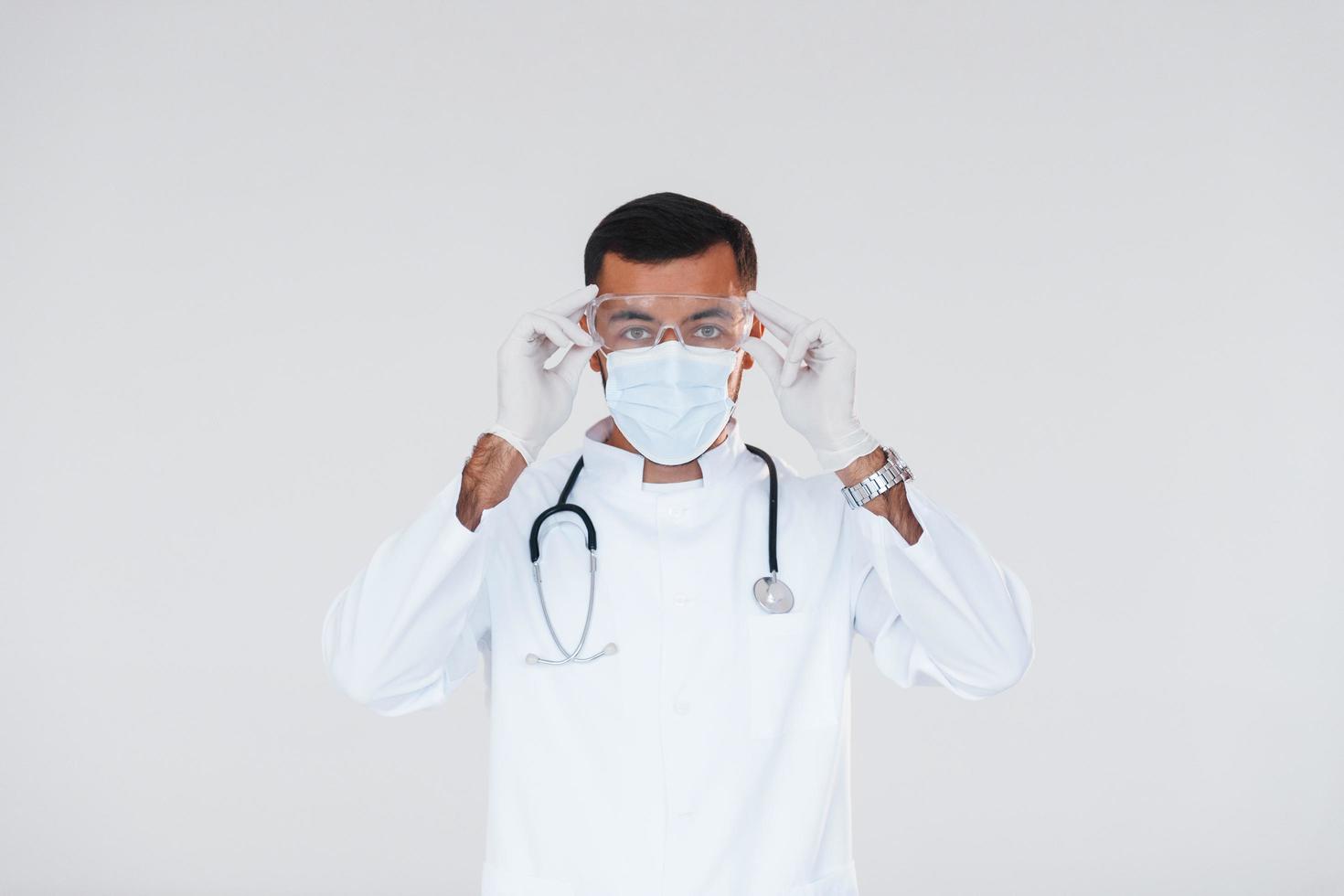 médecin en uniforme. jeune bel homme debout à l'intérieur sur fond blanc photo