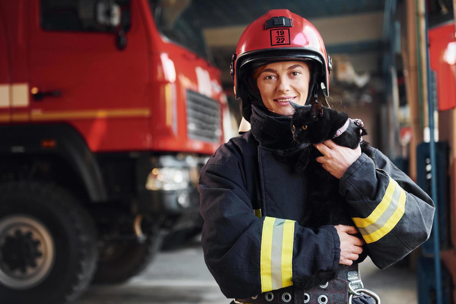 chat noir mignon. femme pompier en uniforme de protection debout près du camion photo