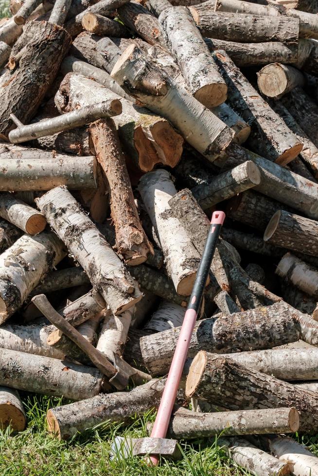 une grande et puissante hache se tient à côté d'un tas de bois de chauffage non coupé, dans la cour d'une maison de village, un jour d'été. photo