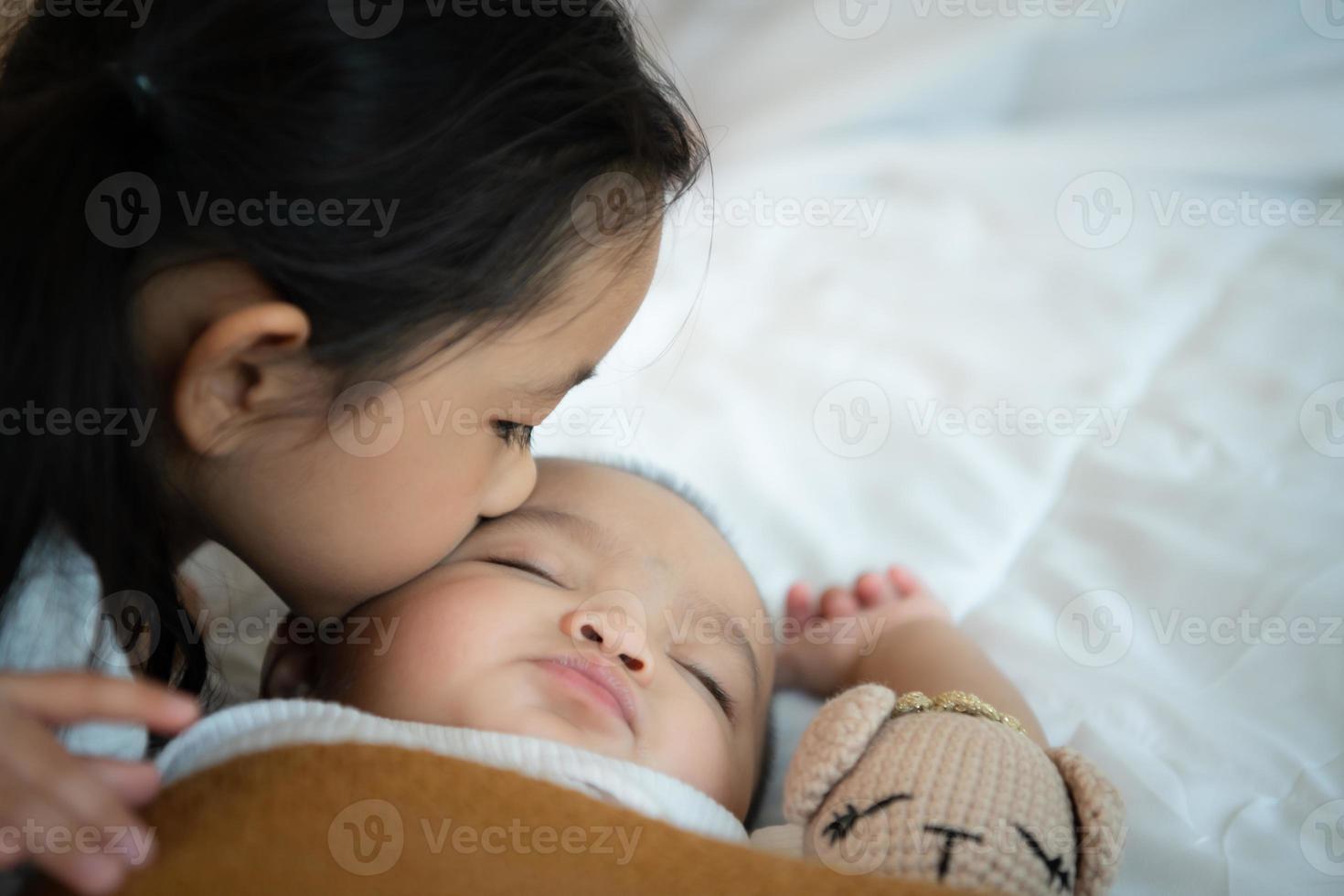 une sœur aînée embrasse sa petite sœur nouveau-née pendant qu'elle dort. dans la chambre blanche photo