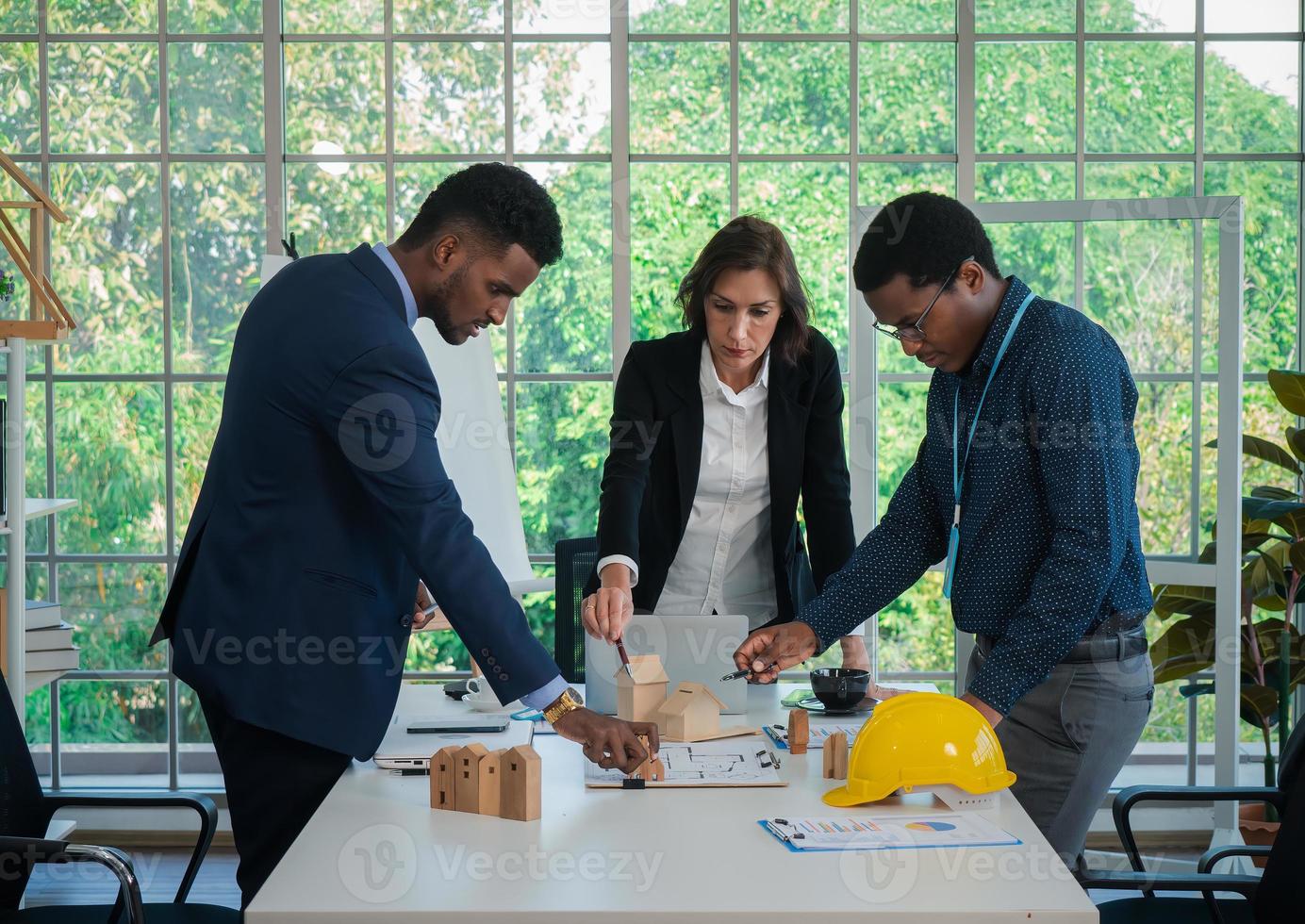 les collègues multiraciaux des hommes d'affaires font un remue-méninges avec des modèles de maison et des plans au bureau. équipe de construction professionnelle discutant de la disposition des lignes de service dans le nouveau bâtiment. photo