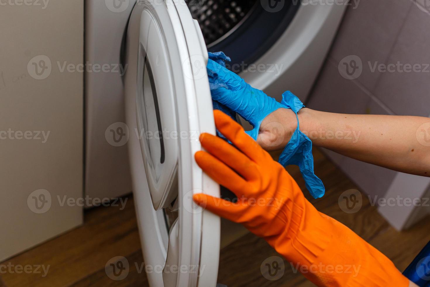 main dans un gant déchiré nettoyant la machine à laver. nettoyage régulier. la femme de chambre nettoie la maison. photo