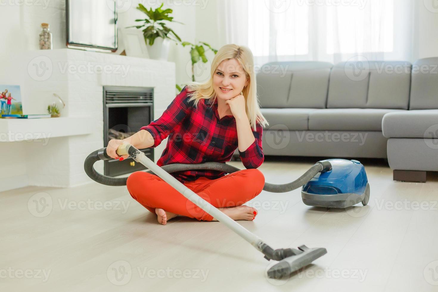 belle jeune femme sourit et utilise un aspirateur tout en nettoyant le sol à la maison photo
