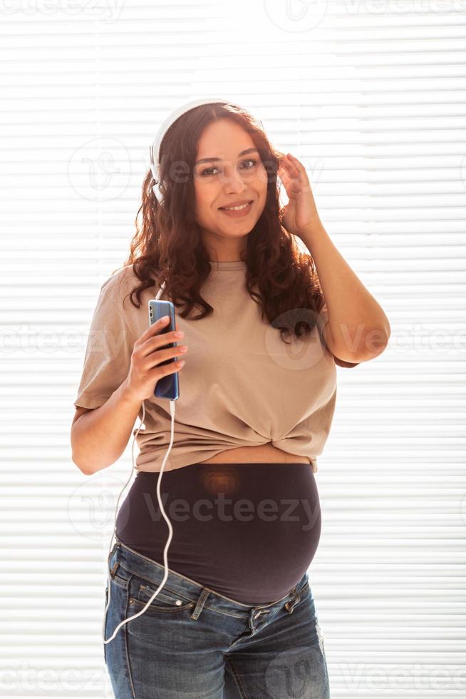 belle jeune femme enceinte paisible écoute de la musique classique agréable à l'aide d'un smartphone et d'un casque. concept d'attitude positive avant l'accouchement photo