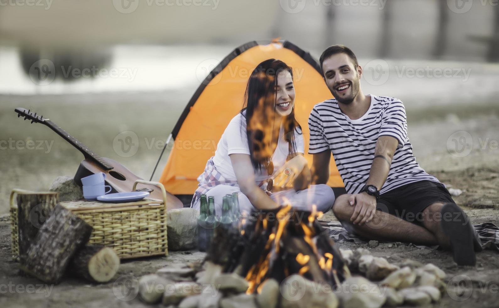 concept de vacances de pique-nique. beau couple s'amusant à faire un barbecue sur un feu de joie et à se détendre au bord d'un lac. photo