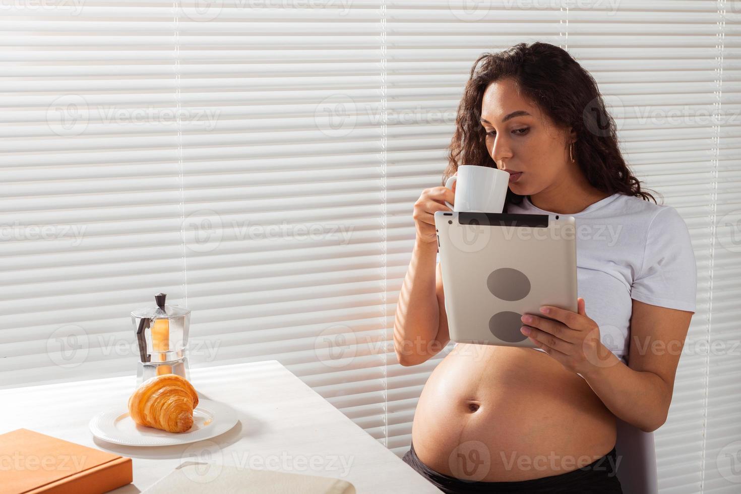 femme enceinte hispanique utilisant une tablette numérique pendant le petit-déjeuner. technologie, grossesse et congé de maternité photo