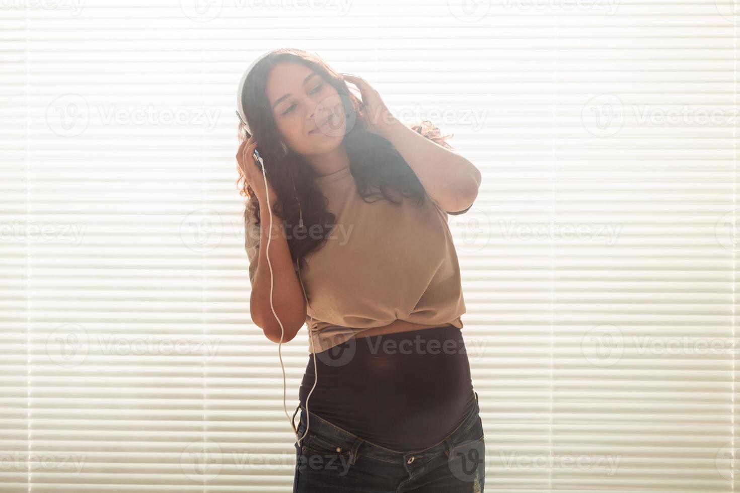 portrait de femme enceinte près de la fenêtre à la maison et écoute de la musique dans des écouteurs avec espace de copie. concept de grossesse et de loisirs. photo