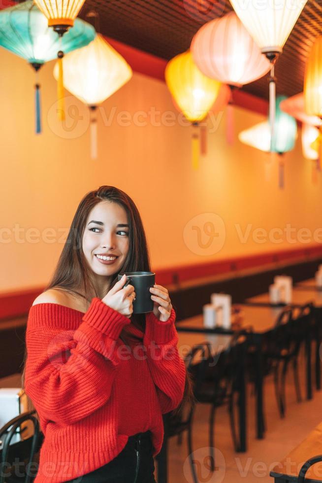 belle jeune femme asiatique souriante en rouge avec une tasse de thé dans le restaurant chinois photo