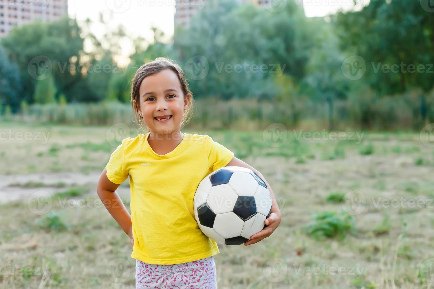 photo en plein air d'une jolie petite fille s'appuyant sur un ballon de football dans l'herbe verte