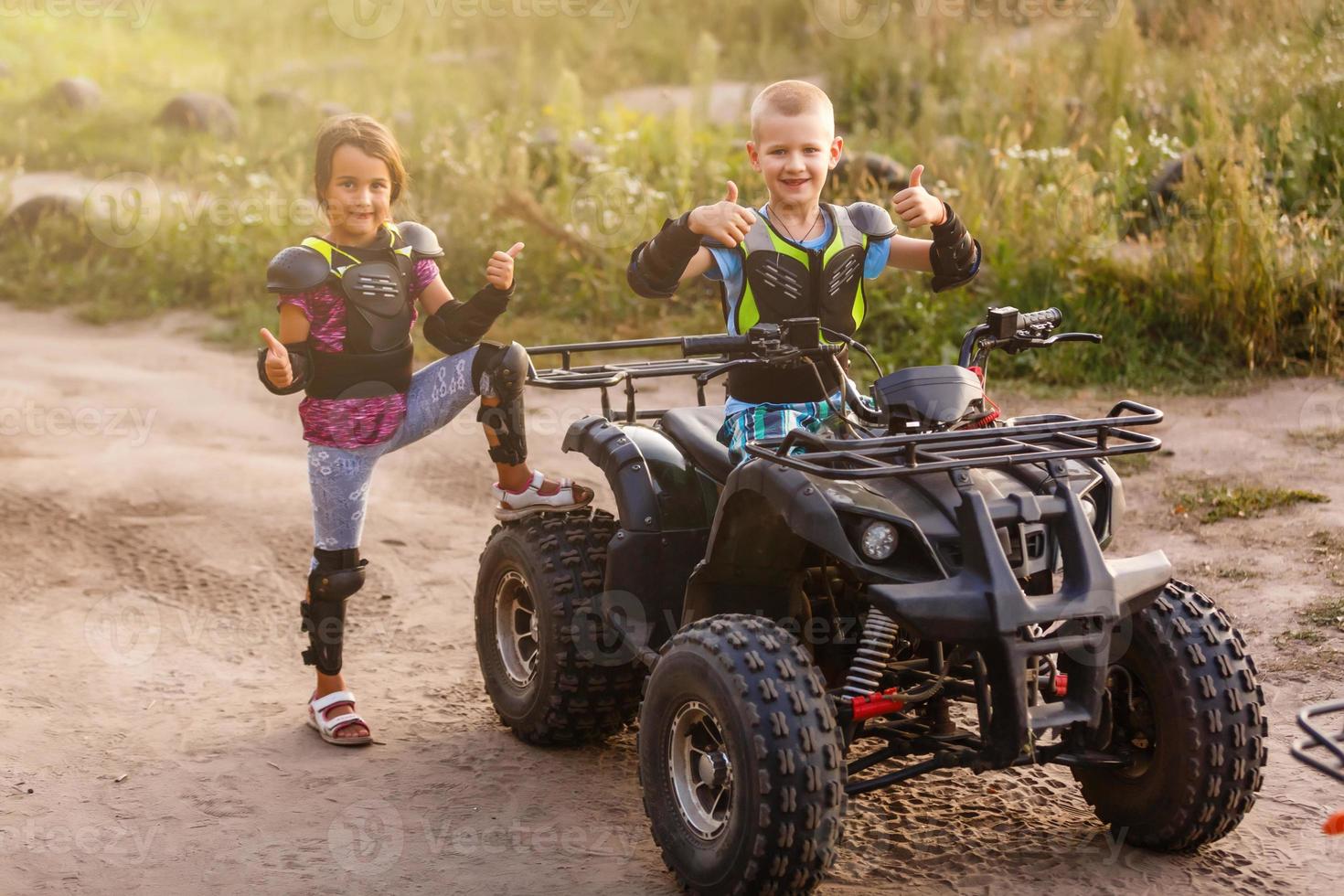 petits enfants heureux jouant sur la route pendant la journée. ils conduisent en quad dans le parc. les enfants s'amusent sur la nature. notion de bonheur. photo