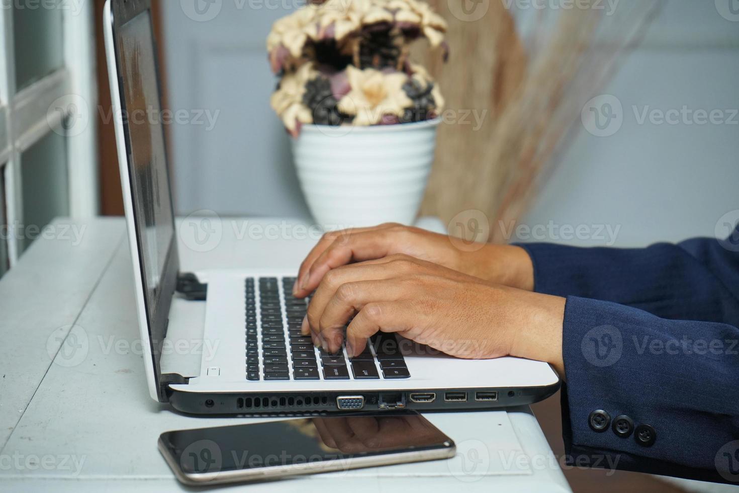 mains d'homme d'affaires asiatique travaillant au bureau avec un ordinateur portable et un téléphone portable, tapant sur le clavier à son bureau, gros plan photo