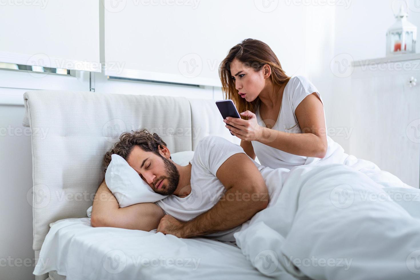 la femme est jalouse et méfiante et espionne le smartphone de son partenaire pendant qu'il dort dans la chambre. la femme espionne le téléphone de son mari pendant qu'il dort. le concept de méfiance, de jalousie photo