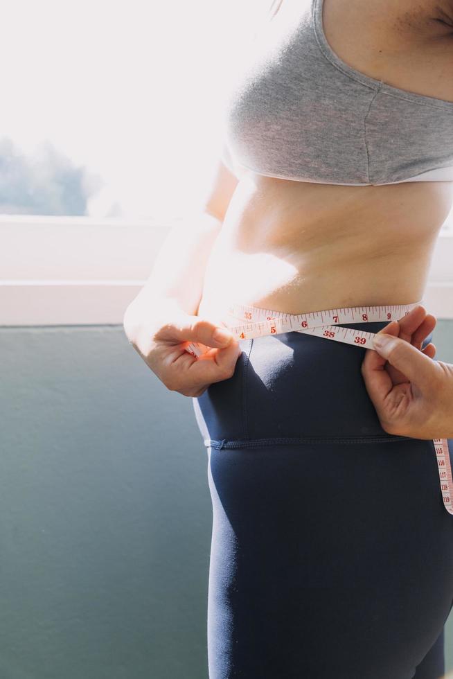 belle grosse femme avec ruban à mesurer, elle utilise sa main pour presser l'excès de graisse isolé sur fond blanc. elle veut perdre du poids, le concept de chirurgie et décomposer les graisses sous le photo