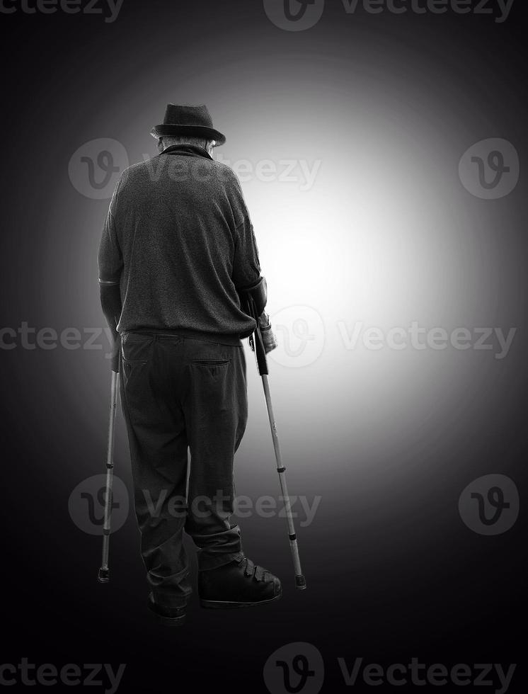 l'homme senior souriant avec deux béquilles se déplaçant de l'obscurité dans le cercle de lumière photo