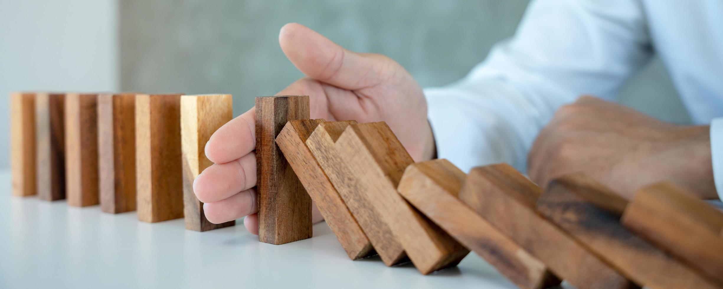 l'assurance avec les mains protège le domino. les mains de l'homme d'affaires empêchent les dominos de tomber dans la crise des affaires. contrôle des risques commerciaux et planification et stratégies pour gérer les entreprises d'assurance. photo