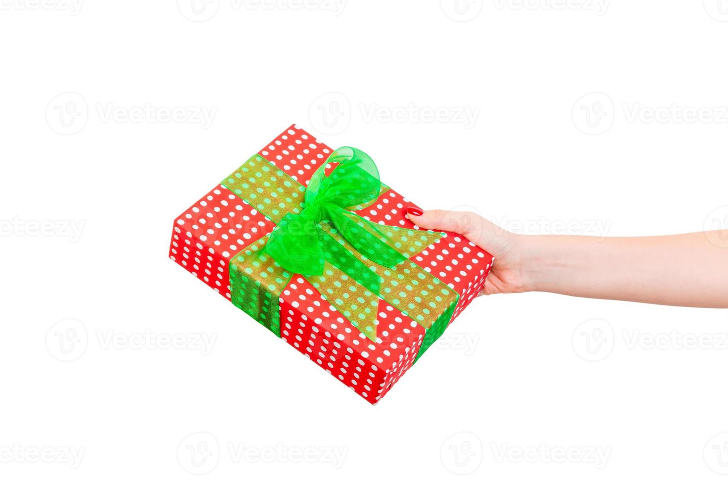 les mains de la femme donnent un noël enveloppé ou d'autres vacances faites à la main dans du papier rouge avec un ruban vert. isolé sur fond blanc, vue de dessus. concept de boîte-cadeau d'action de grâces photo