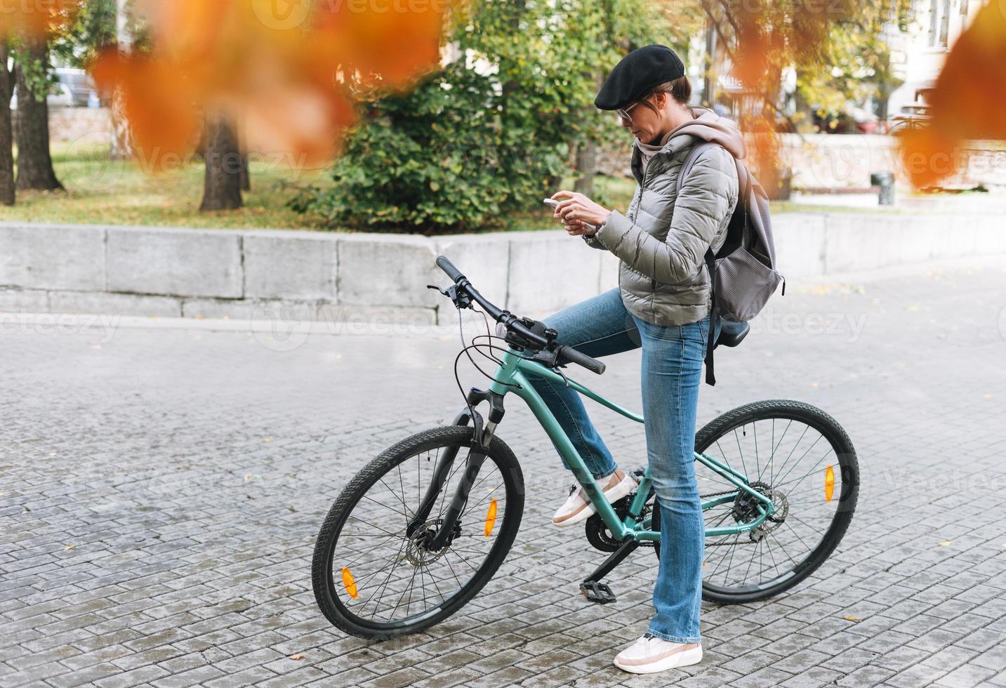 portrait d'une jolie jeune femme à la mode en casquette et lunettes de soleil à l'aide de mobile à vélo le jour ensoleillé d'automne dans le parc de la ville photo