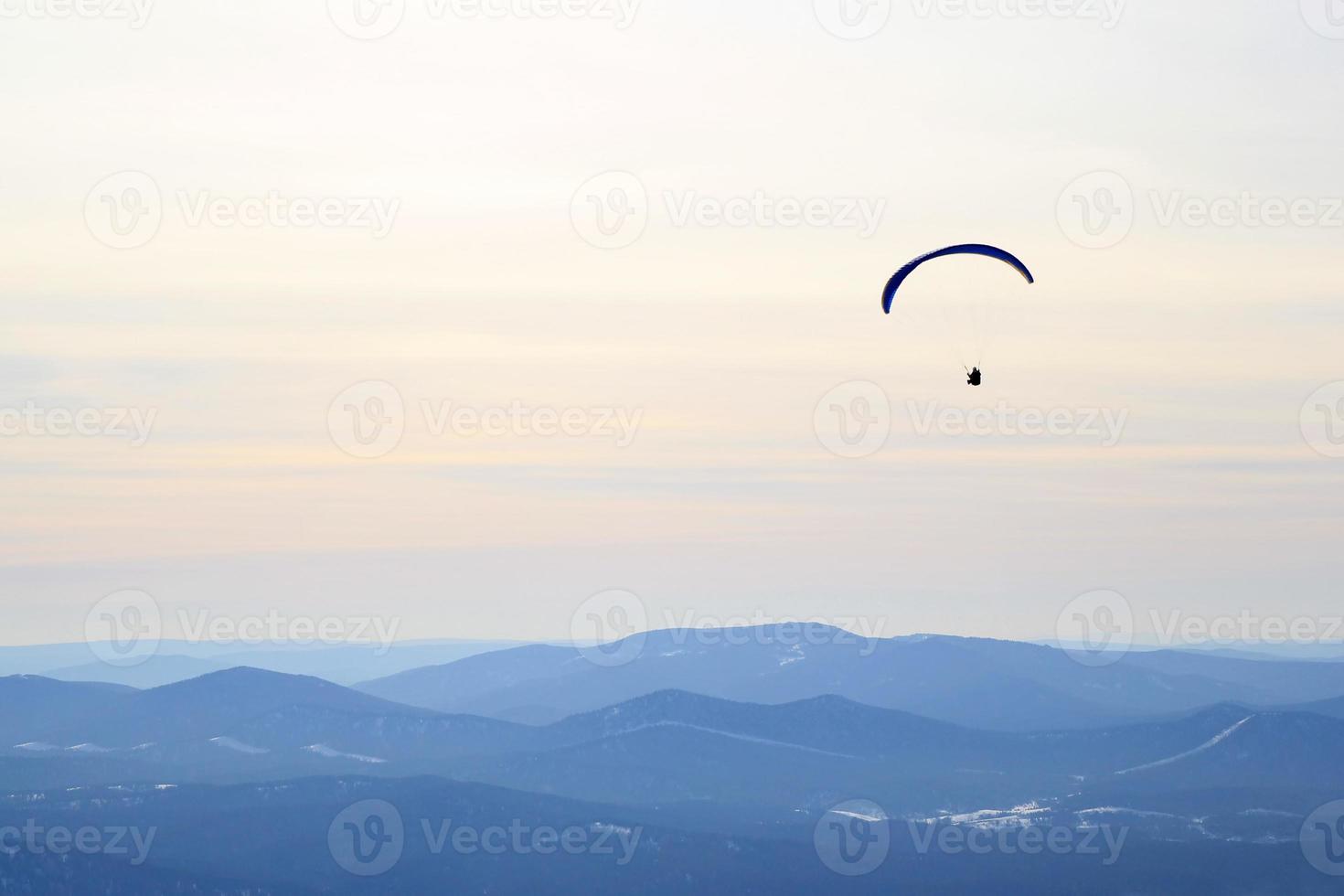 voyage à sheregesh, russie. le parapente vole dans le ciel au-dessus des montagnes. paysage d'hiver. photo