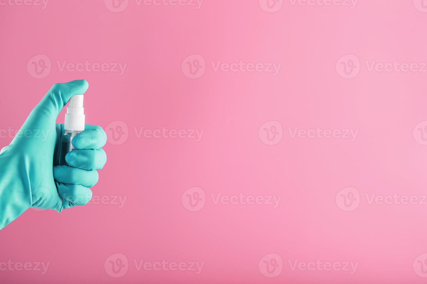 une main gantée de bleu tient un désinfectant sur fond rose. traitement antiseptique des mains à partir d'un désinfectant bactérien. photo