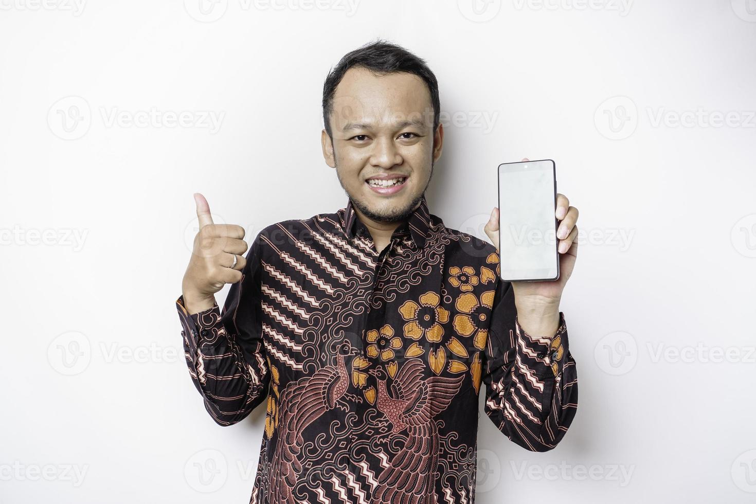 portrait d'un homme asiatique souriant portant une chemise batik et montrant un écran vert sur son téléphone, isolé sur fond blanc photo