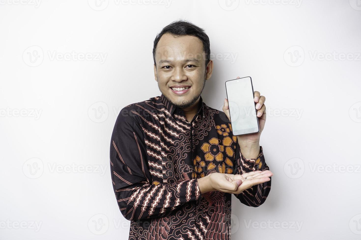 portrait d'un homme asiatique souriant portant une chemise batik et montrant un écran vert sur son téléphone, isolé sur fond blanc photo