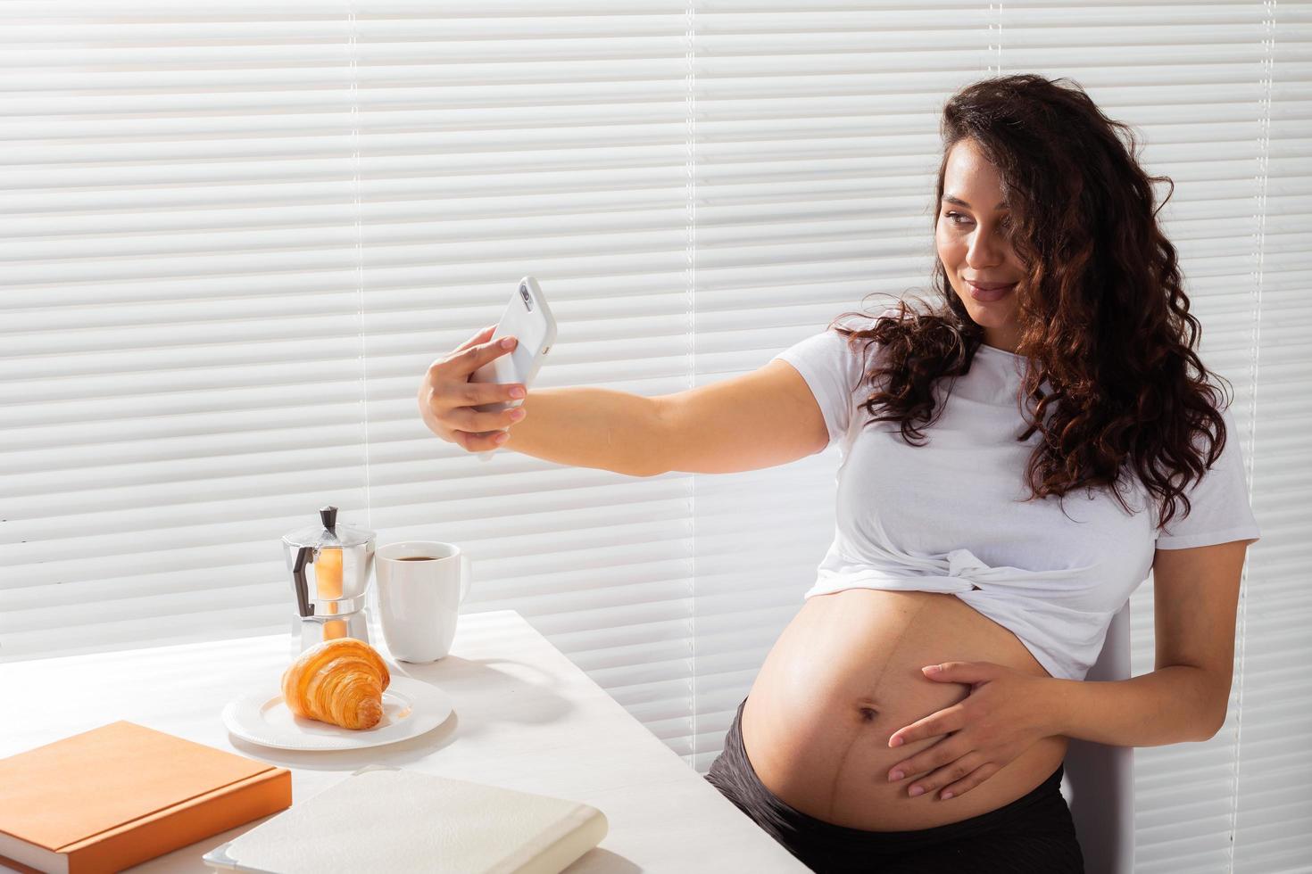 femme enceinte prenant un autoportrait avec son smartphone pendant le petit-déjeuner photo