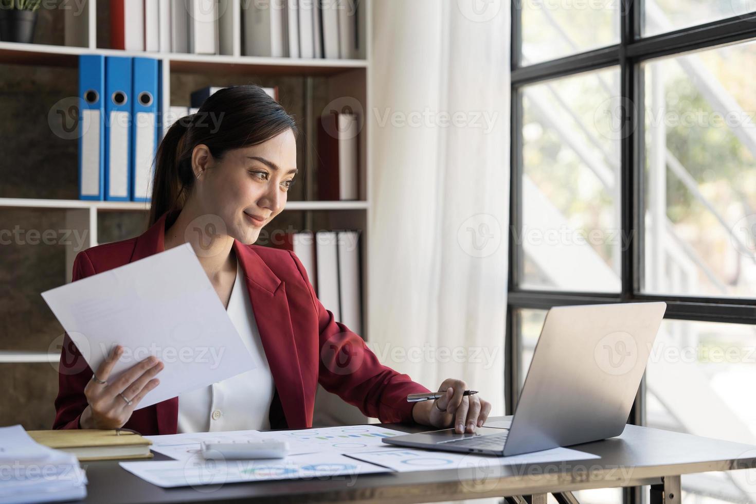 sourire jolie femme asiatique d'affaires travaille son travail sur un ordinateur portable dans un bureau moderne. faire un rapport d'analyse comptable données d'investissement immobilier, concept de systèmes financiers et fiscaux photo