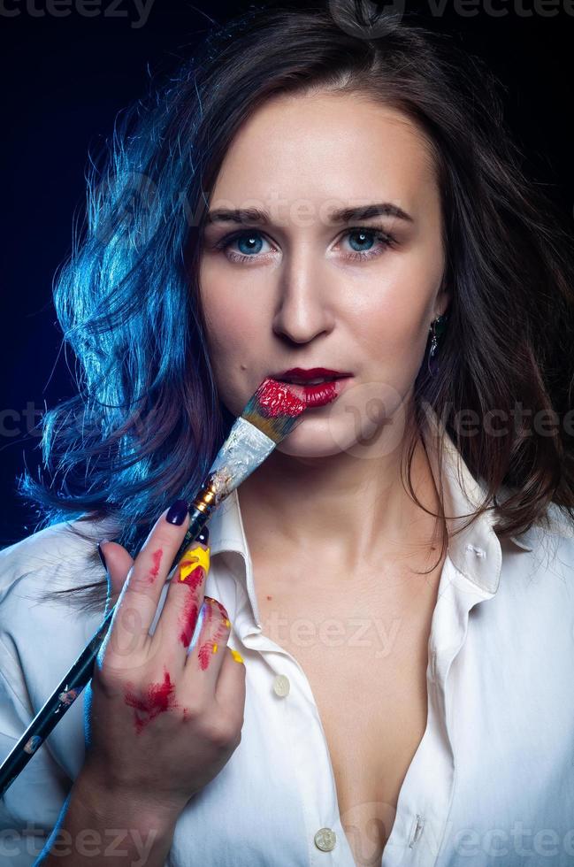 la maquilleuse met du rouge à lèvres. beau visage féminin. la main d'un maquilleur, peignant les lèvres d'un beau jeune mannequin. maquillage en cours photo