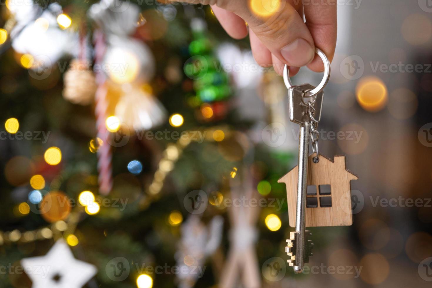 la clé de la maison avec un porte-clés est accrochée au sapin de noël. un cadeau pour le nouvel an, noël. construction, conception, projet, déménagement dans une nouvelle maison, hypothèque, location et achat immobilier. copie espace photo