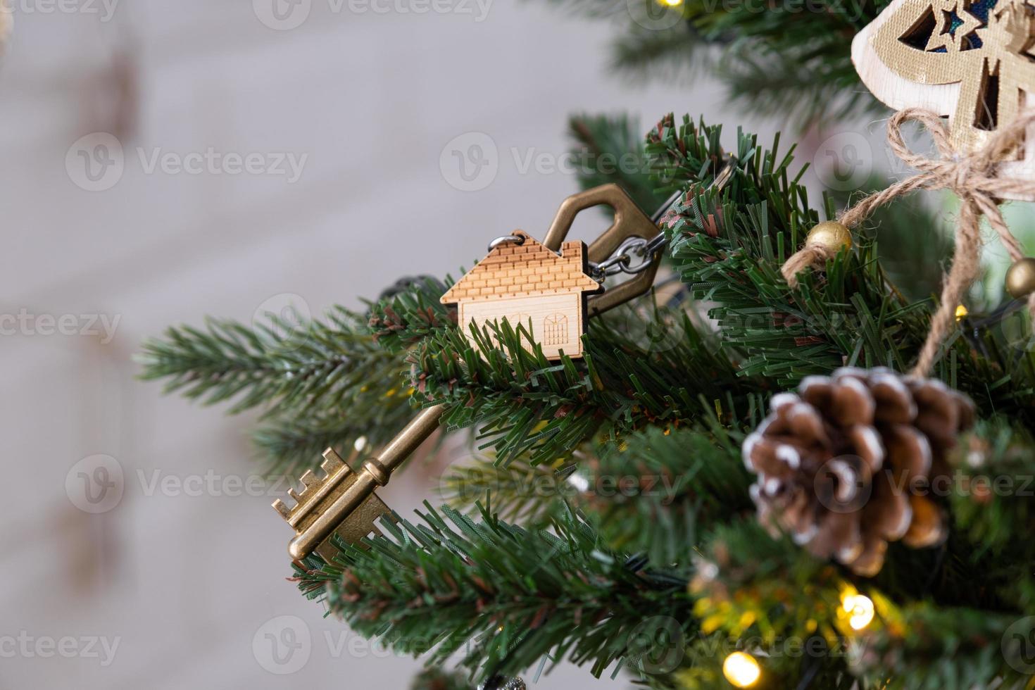 la clé de la maison avec un porte-clés est accrochée au sapin de noël. un cadeau pour le nouvel an, noël. construction, conception, projet, déménagement dans une nouvelle maison, hypothèque, location et achat immobilier. copie espace photo