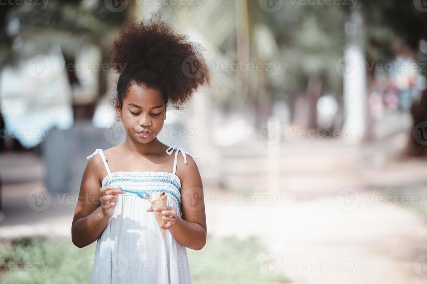 petite fille afro-américaine mangeant un cornet de crème glacée dans le parc extérieur photo