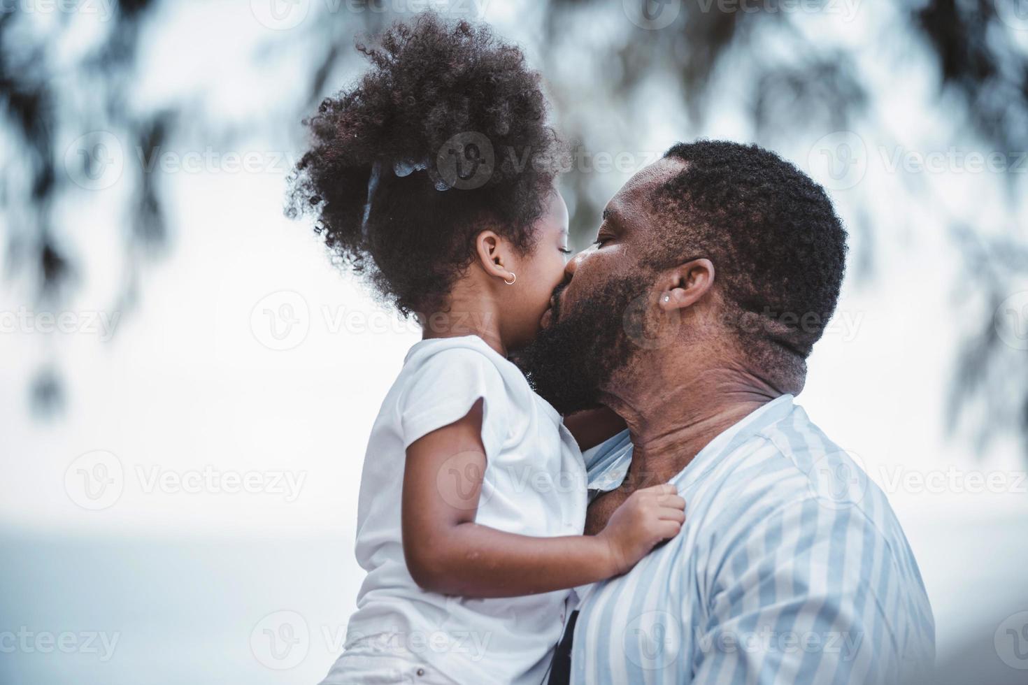 père afro-américain portant sa fille et bisous sur la joue avec un amour joyeux. famille heureuse. photo