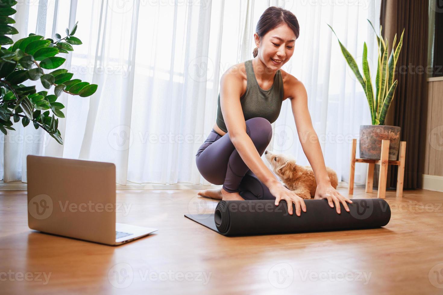 jeune femme asiatique déroulant un tapis de yoga noir avec son chien à la maison, nouveau concept de mode de vie normal photo