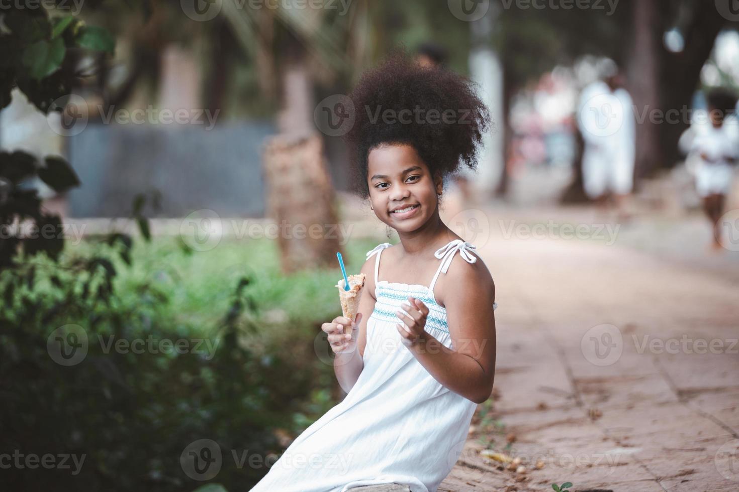 jolie petite fille afro-américaine mangeant un cornet de crème glacée dans le parc extérieur photo