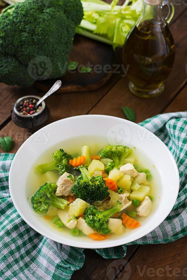 soupe au poulet avec brocoli, pois verts, carottes et céleri dans un bol blanc sur fond de bois de style rustique photo