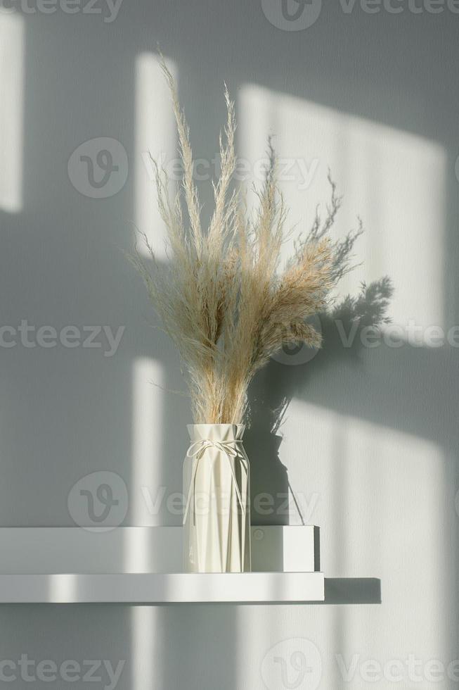 décor floral intérieur de la maison. fleurs séchées dans un vase sur une étagère blanche. fond avec des lumières d'ombre. photo