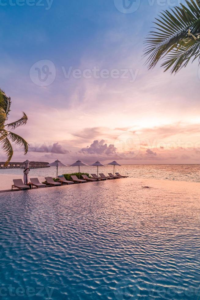 parasol et chaise autour de la piscine à débordement près de la plage de l'océan au lever ou au coucher du soleil. pour les voyages d'agrément et le concept de vacances, paysage de station balnéaire. vacances de détente tropicale, coucher de soleil photo