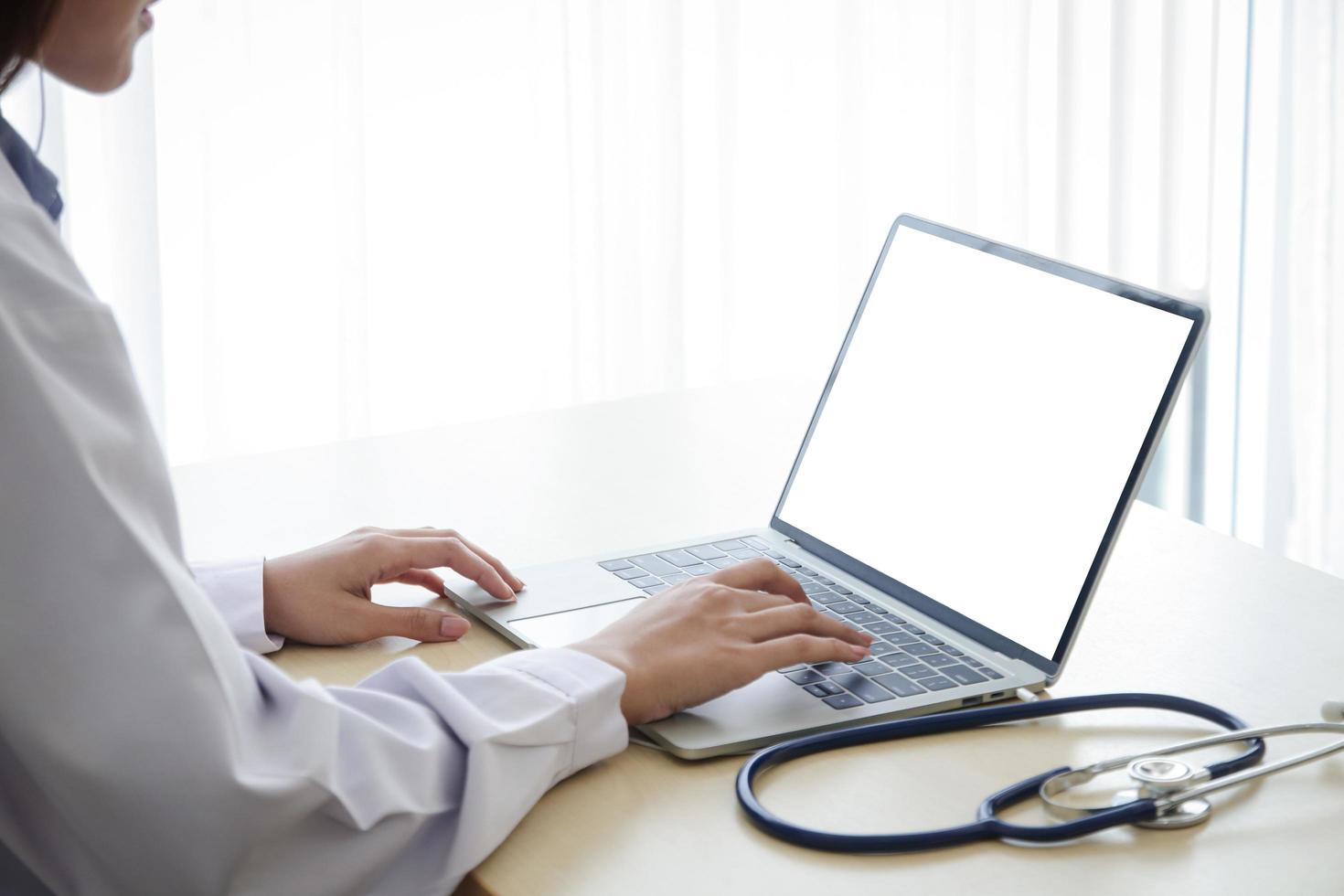 une femme médecin au travail a tapé des informations sur un ordinateur portable à écran blanc. concept de communication technologique en ligne. les médecins peuvent examiner les patients par le biais d'appels vidéo. chemin de détourage photo