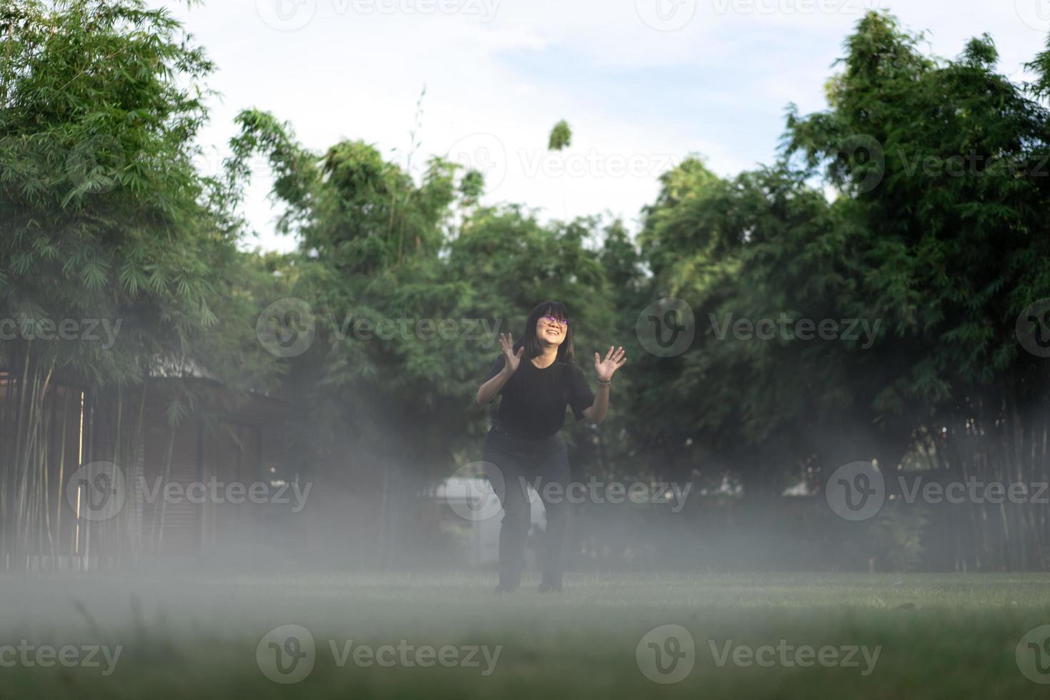 la femme asiatique aux cheveux courts est joyeuse en sautant dans l'environnement de brouillard sur le jardin de terrain en herbe. photo
