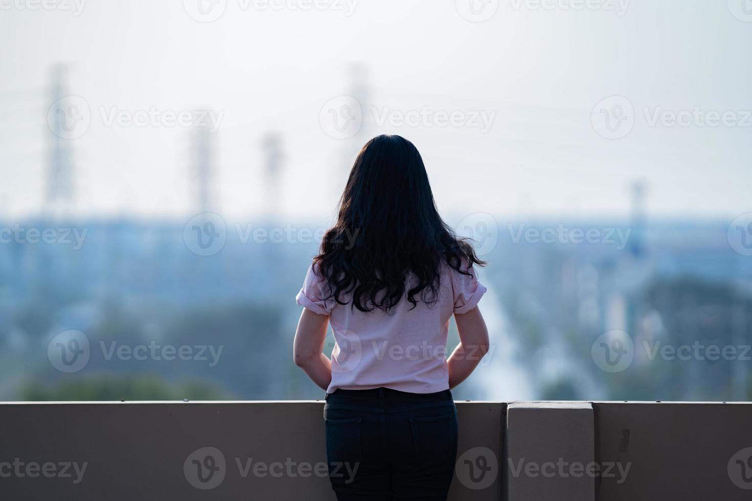 une adolescente asiatique se tient à l'arrière devant la vue sur la ville sur le toit de l'immeuble photo